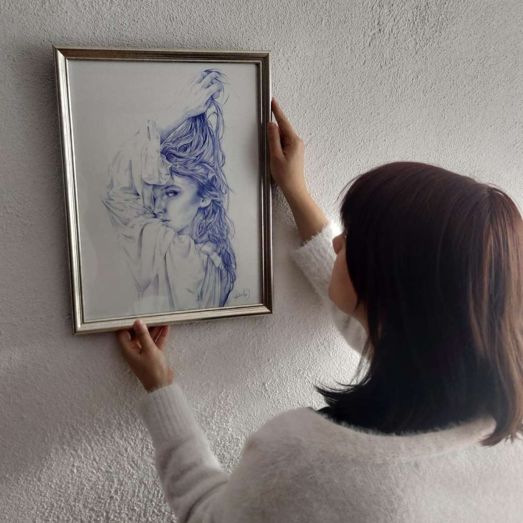 Obra Amanecer Salvaje de Christine Hope siendo colocada en la pared por una mujer, enmarcada en tono plateado.